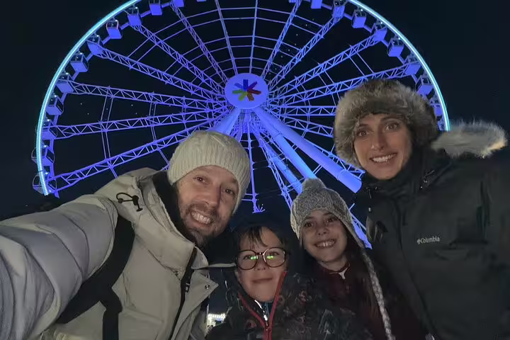 Family selfie by the illuminated Montreal observation wheel during a scavenger hunt city highlights walking tour