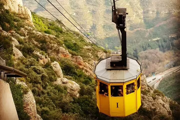 Yellow cable car ascending Montserrat mountain, offering stunning views on a 2-day Gaudi, Sagrada Familia, and winery tour.