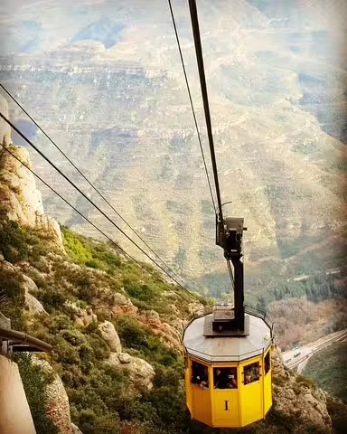 Yellow cable car ascending Montserrat Mountain, offering scenic views, part of a private tour with lunch and wine tasting in Penedes.
