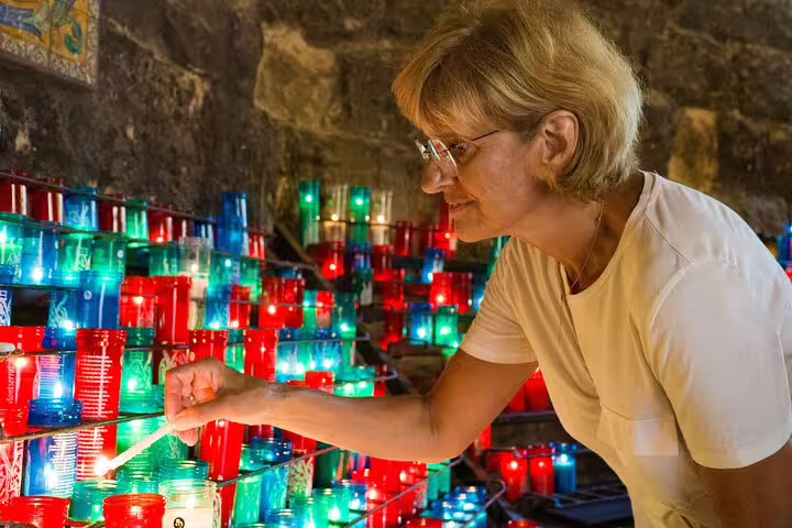A woman lights a candle in Montserrat's chapel, part of a full-day tour featuring a farmhouse lunch and winery visit.