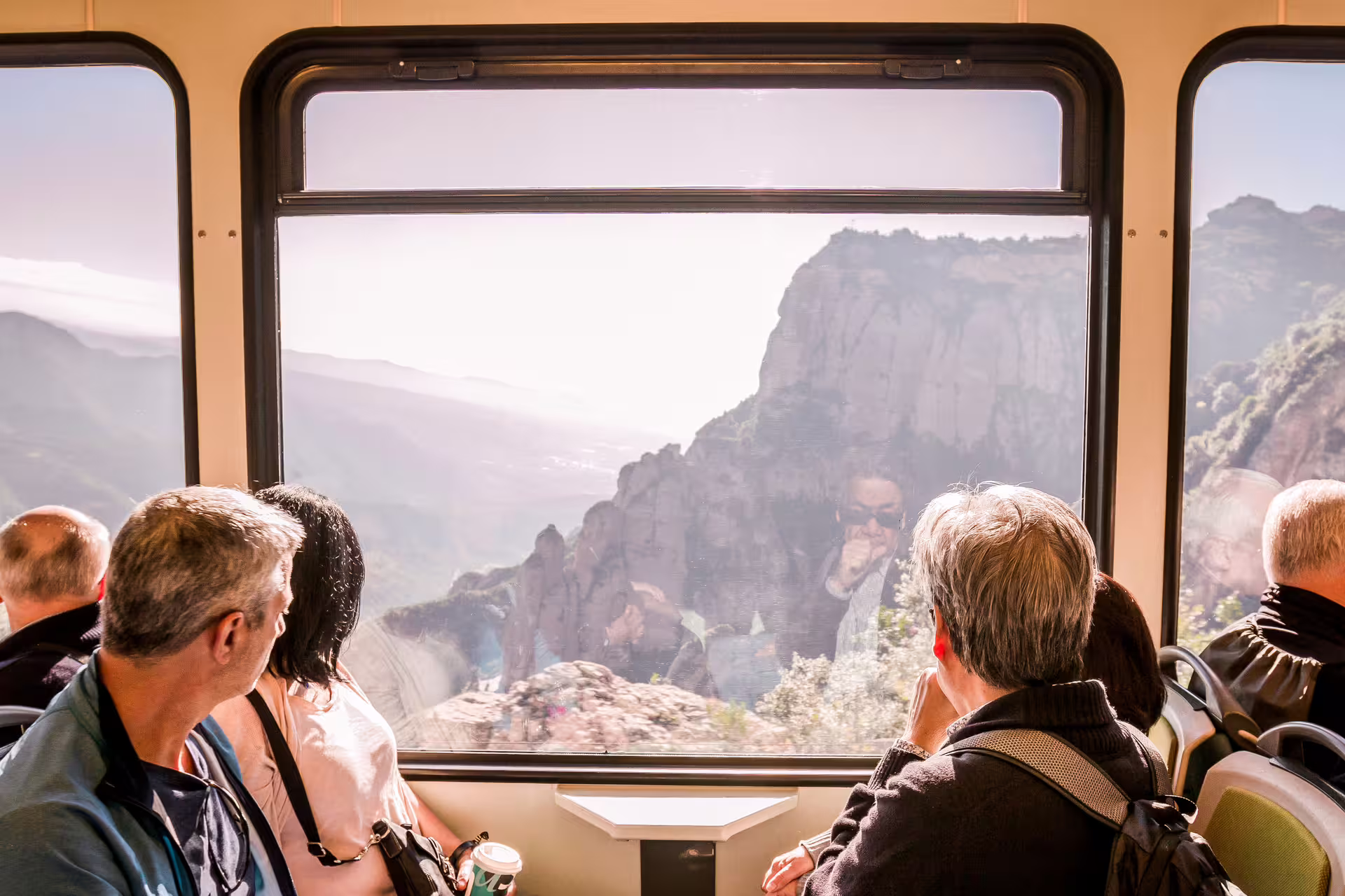 Tourists enjoy scenic views of Montserrat's rugged landscape from a cogwheel train, highlighting the Extended Montserrat, Tapas & Wine tour.
