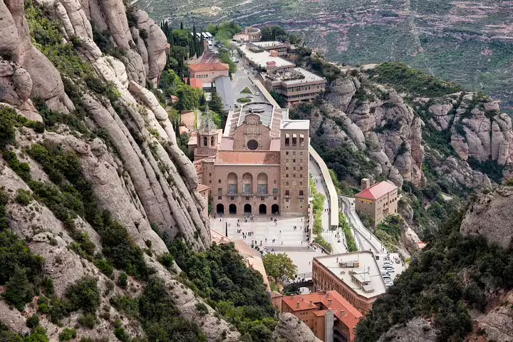 Aerial view of Montserrat Monastery nestled in rugged mountains, a highlight of the Barcelona tour with convenient hotel pickup.
