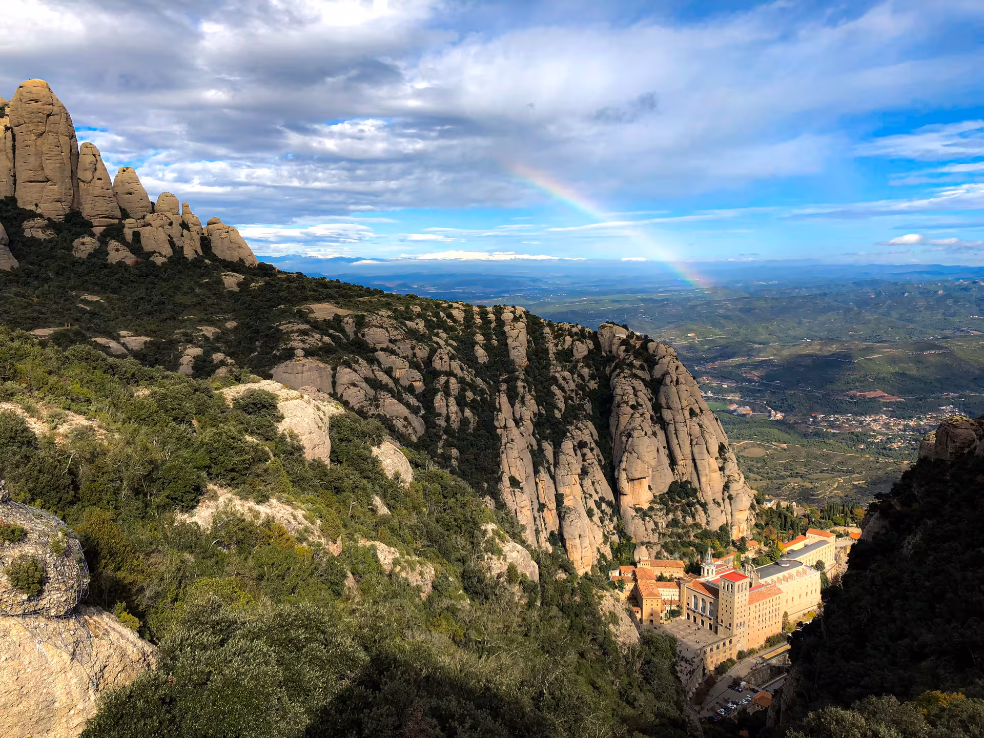 Montserrat mountain viewpoint with monastery below and rainbow, private half-day tour from Barcelona by vehicle
