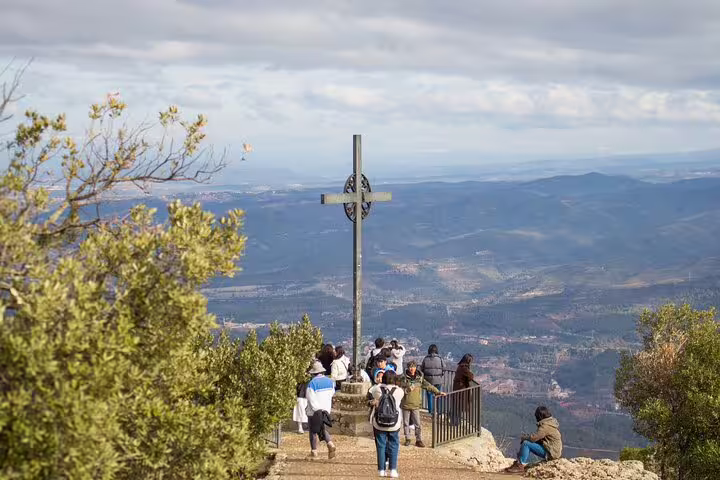 Tourists enjoying panoramic views from a cross viewpoint on Montserrat mountain, capturing stunning landscapes.