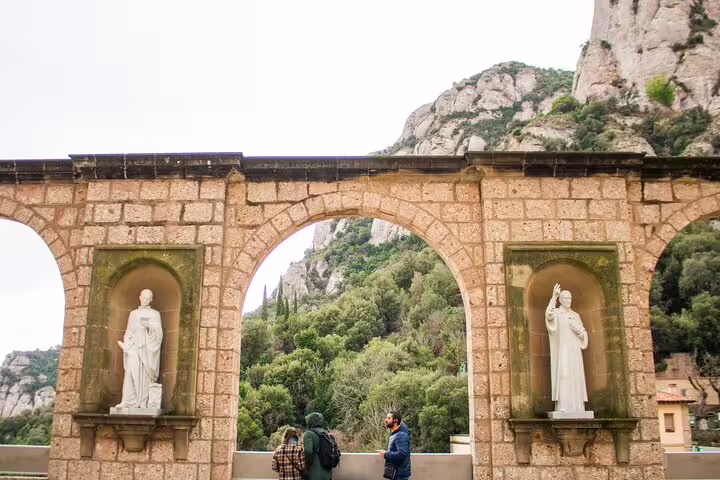 Historic stone arches with statues at Montserrat, surrounded by lush greenery on the full-day tour with lunch and winery visit.