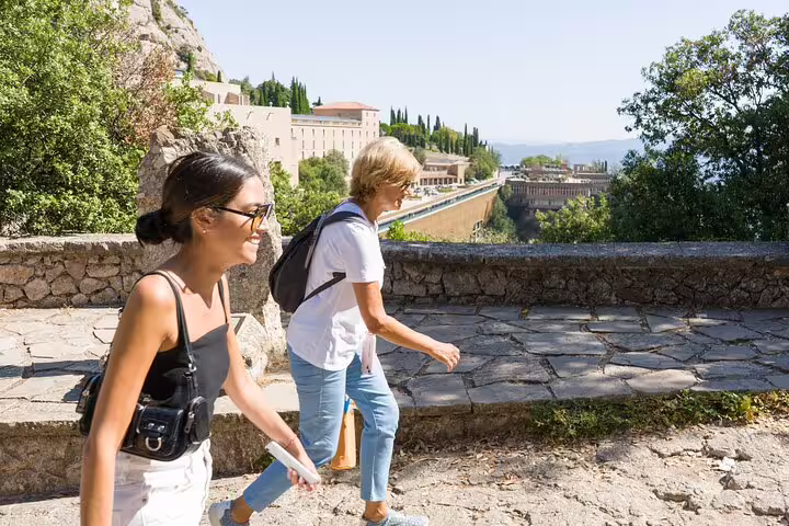 Visitors smiling as they explore the picturesque Montserrat path, surrounded by lush greenery and historic buildings.