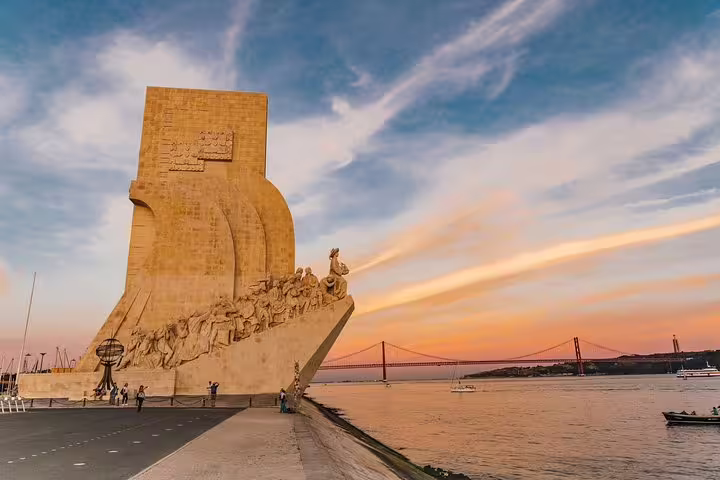 The Monument to the Discoveries at sunset with the 25 de Abril Bridge in the background, located in Belém, Lisbon.