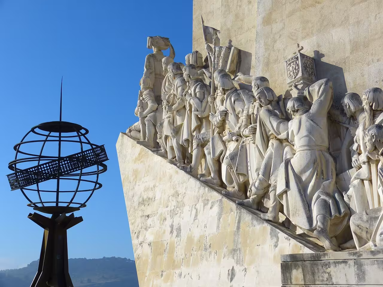 Close-up of the Monument to the Discoveries with detailed sculptures under a clear blue Lisbon sky.