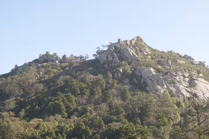 Breathtaking view of the ancient Moorish Castle atop lush green hills in Sintra, Portugal, under a clear blue sky.