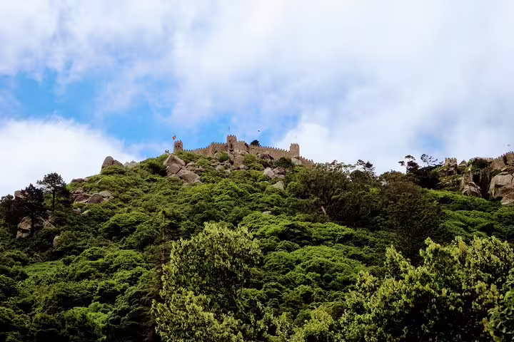 Lush greenery and ancient stone walls of the Moorish Castle in Sintra, Portugal, under a bright blue sky on a heritage tour.
