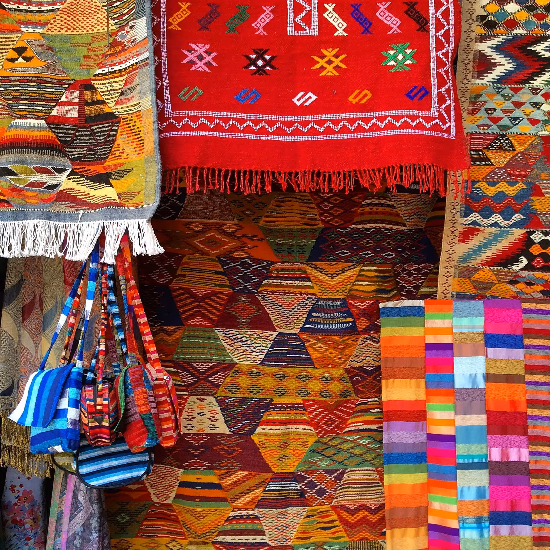 Colorful Moroccan Berber rugs and woven bags in a souk market, Timeless Morocco cultural tour