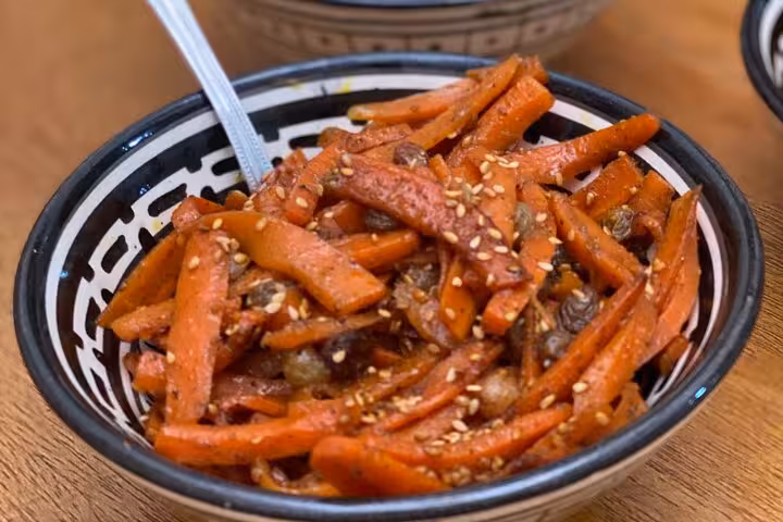 Close-up of Moroccan carrot salad with sesame seeds and raisins in a decorative bowl, showcasing vibrant textures.