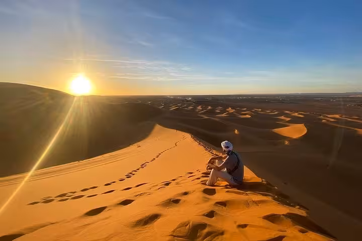 Tour participant watching a breathtaking sunset over Morocco’s desert dunes, part of the Fes luxury tour experience.