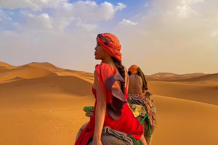 Traveler in desert scarf on camel in Merzouga dunes at sunset, Morocco 12 days tour from Casablanca itinerary