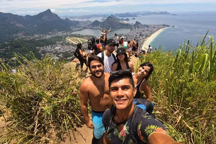 Smiling group of hikers atop Two Brothers Mountain, overlooking Rio's breathtaking landscape and ocean views.