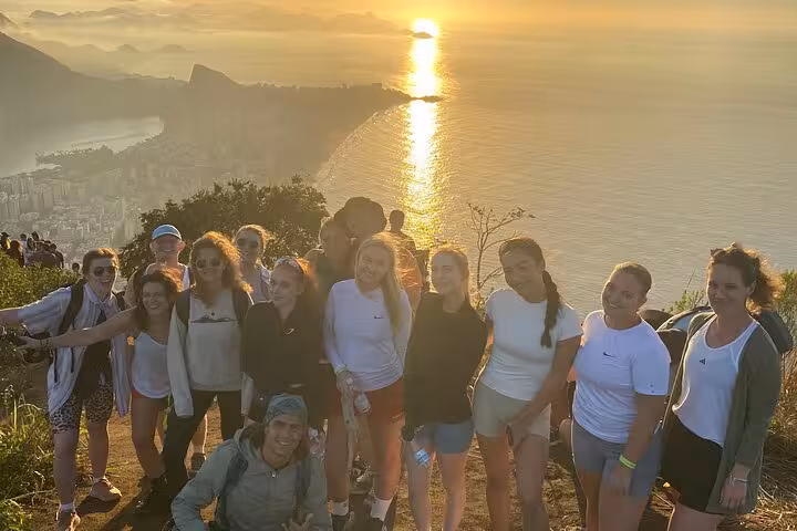 A group of hikers poses at sunset on Vidigal with a stunning view of Rio's coastline, capturing the vibrant spirit of Brazil.