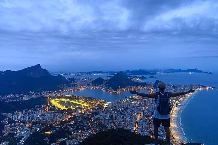 Traveler embracing the night view of Rio's coastline from Two Brothers hike, showcasing Vidigal's stunning cityscape.