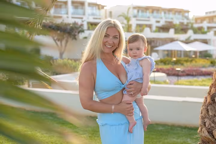 Mother in a light blue dress holding her baby in a scenic garden during a private photoshoot in Analipsi.