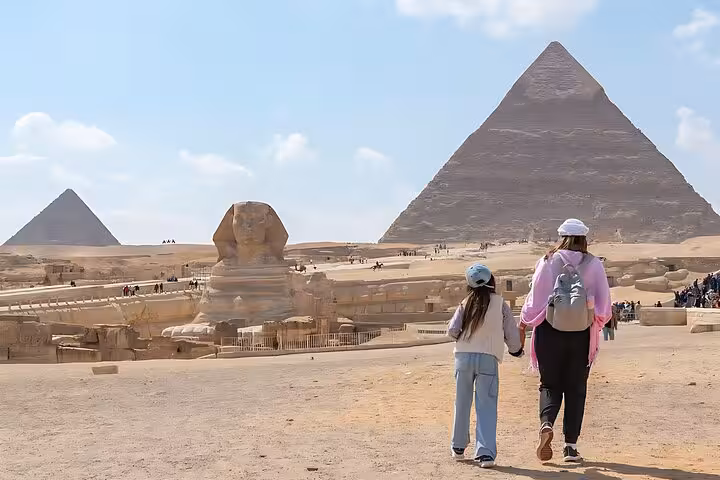 Mother and child walking toward the Great Sphinx and Giza pyramids on Cairo day trip to Sakkara and Memphis