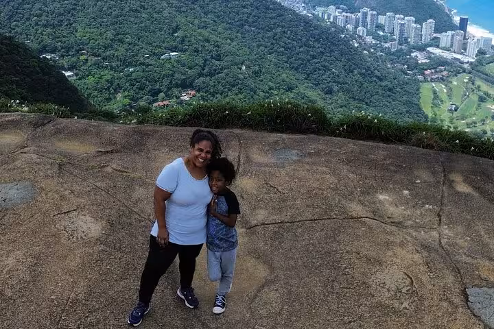 Mother and child smiling on a stone trail with lush forest and city views in DA Tijuca Forest.