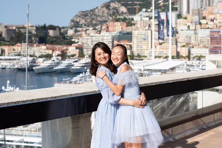Mother and daughter in elegant dresses embrace with scenic Cannes marina backdrop during private photoshoot.