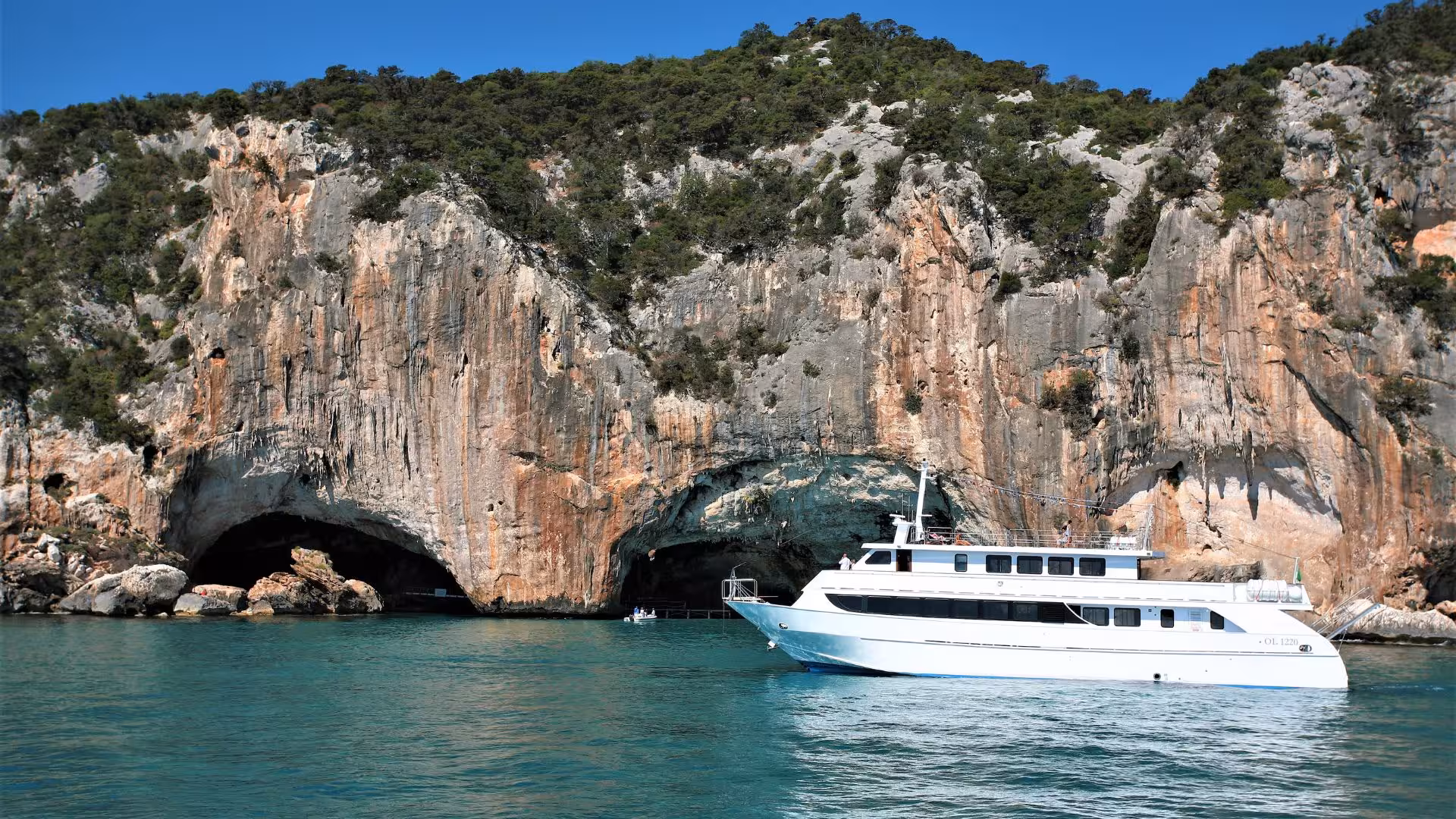 White motorboat near the entrance of Bue Marino Caves with dramatic rocky cliffs in Cala Gonone.