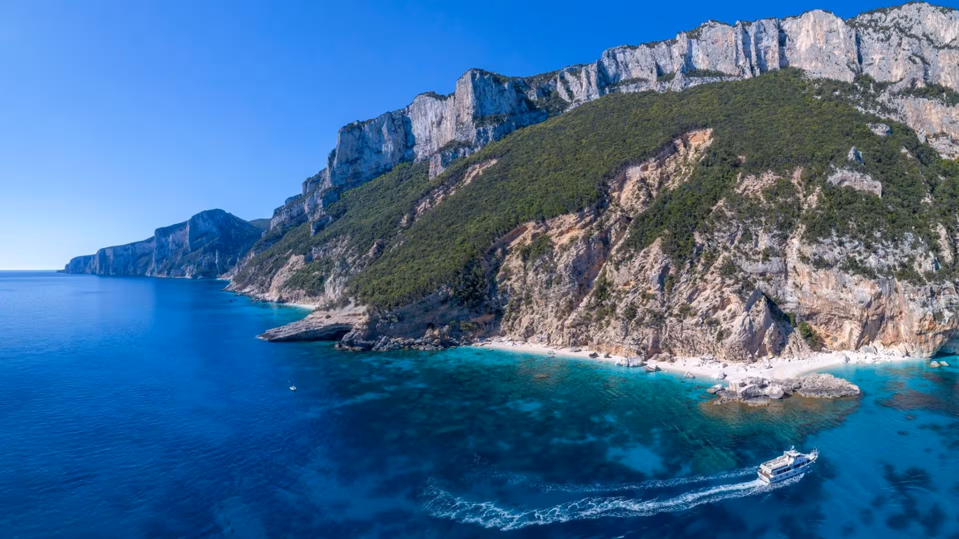 Aerial view of a motorboat near the stunning cliffs and azure waters of the Gulf of Orosei, Sardinia.