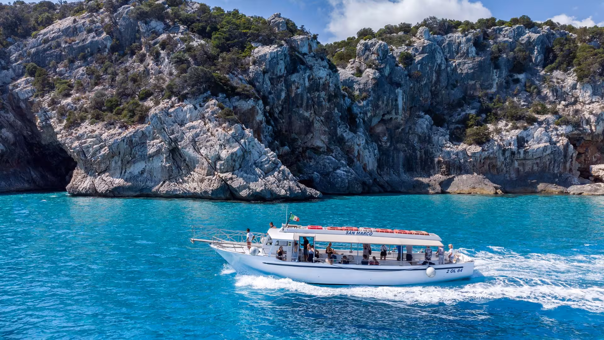 Motorboat cruising along turquoise waters with rocky cliffs in the Gulf of Orosei, Sardinia, on a sunny day.