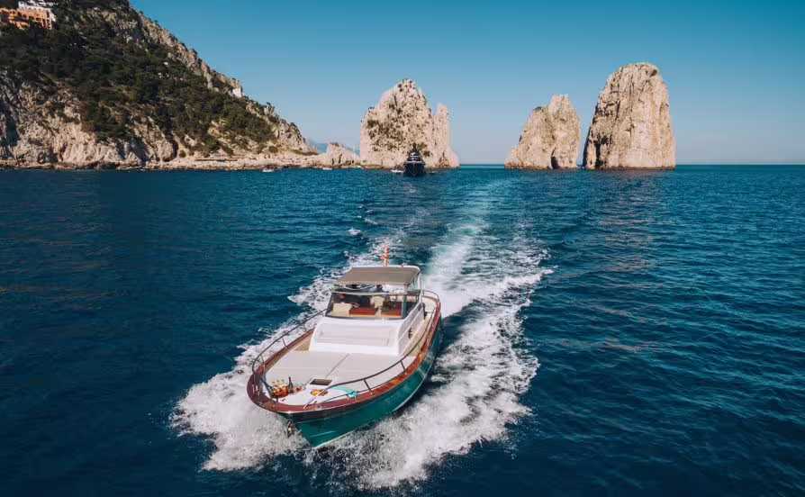 Motorboat touring around Capri with wake trail leading toward the iconic Faraglioni rock formations in Italy
