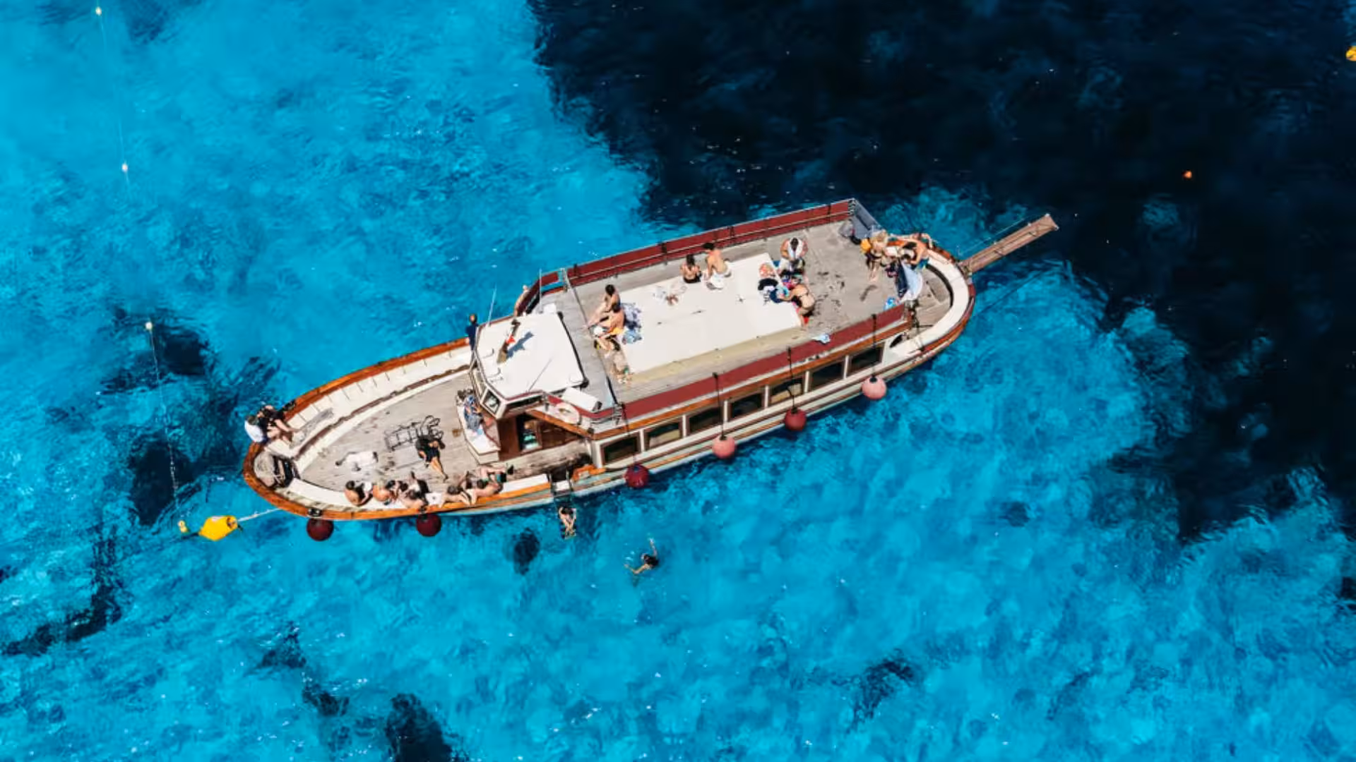 Top view of a motorboat with tourists enjoying the sun on crystal-clear waters in La Maddalena Archipelago tour.