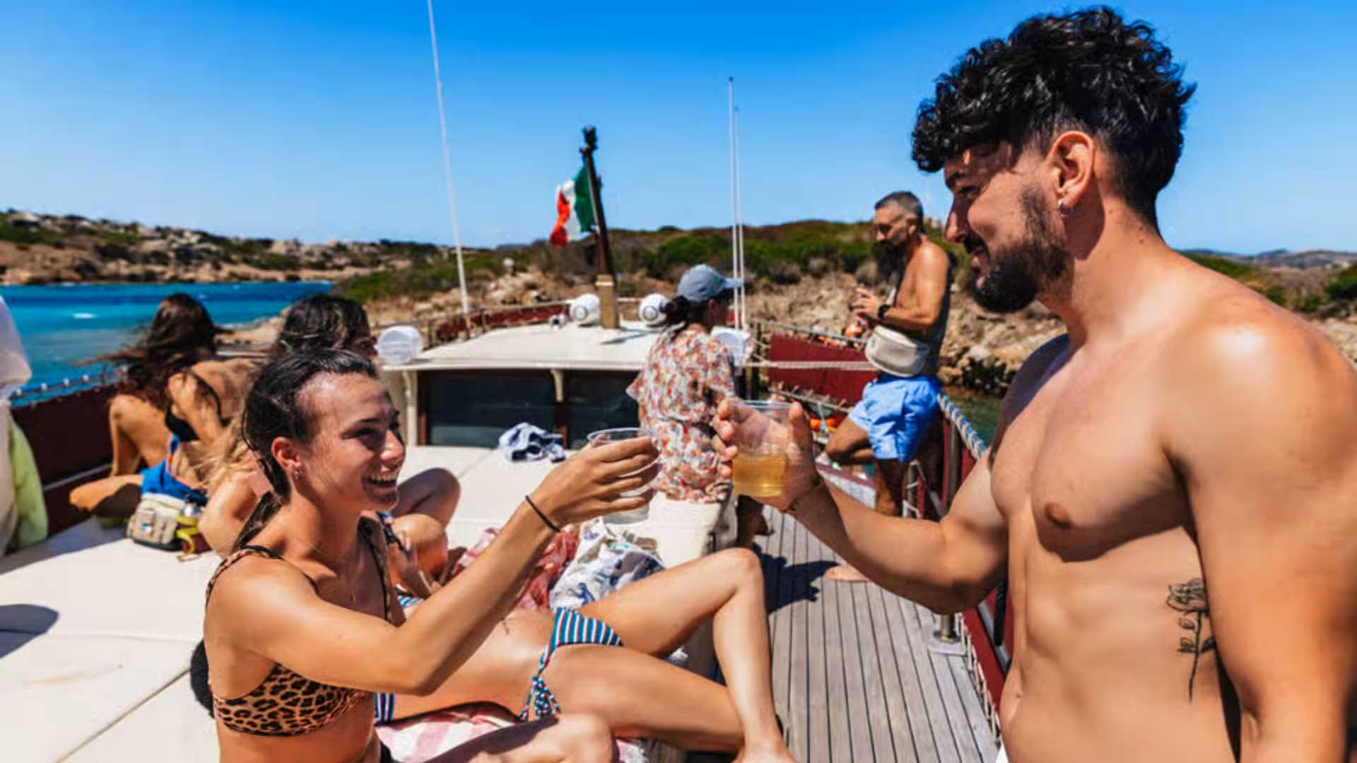 Tour guests toasting with drinks on a sunlit motorboat deck exploring the La Maddalena Archipelago.
