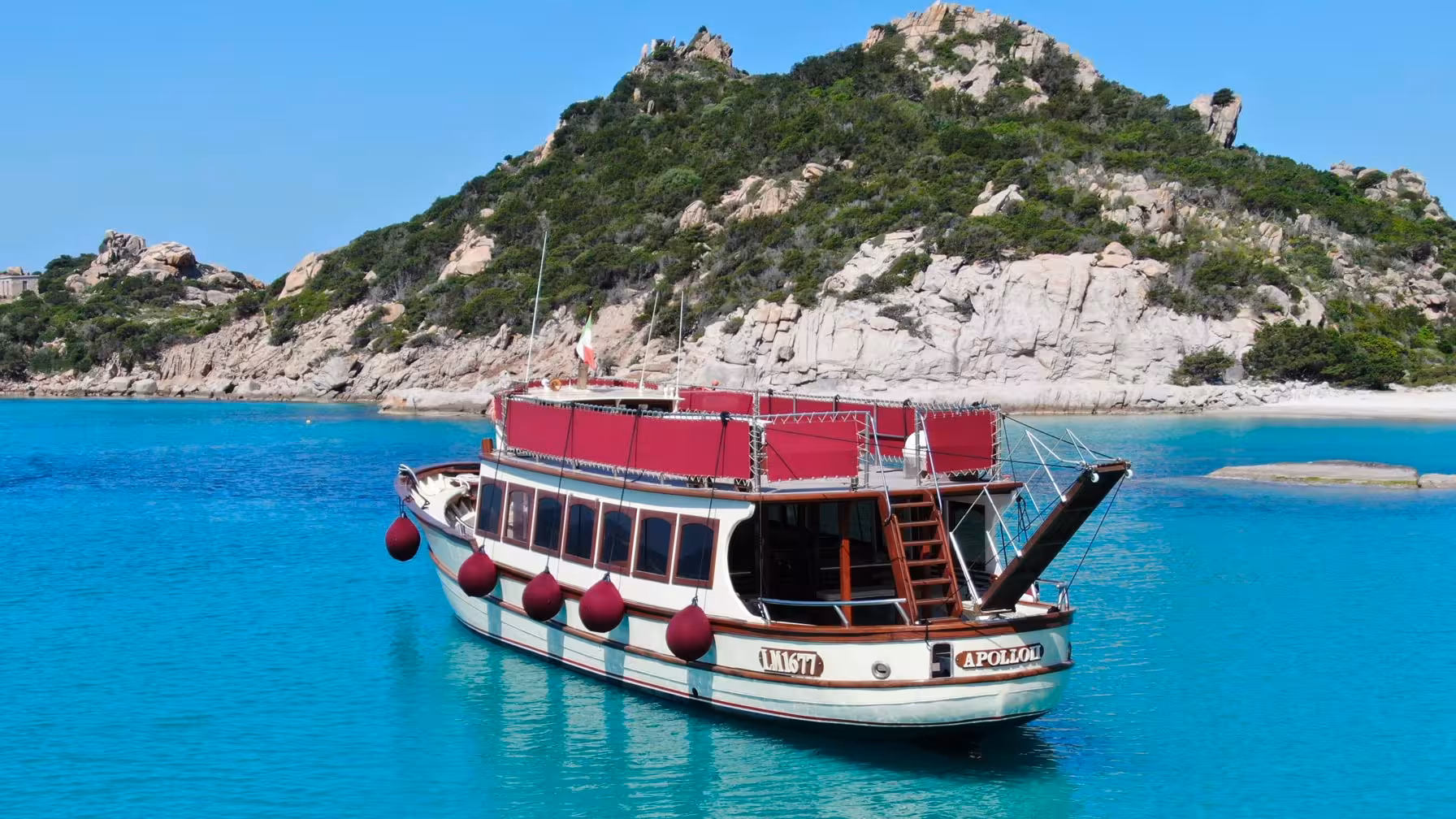 Motorboat anchored in turquoise waters near a lush island in La Maddalena Archipelago, perfect for scenic tours.