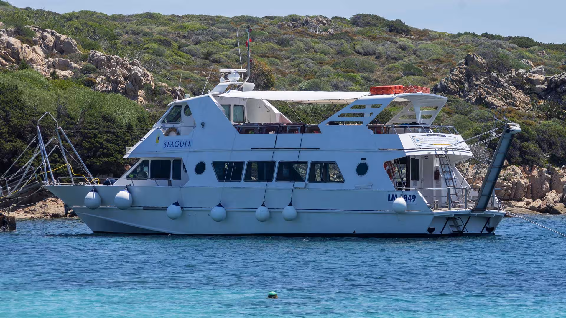 White motorboat docked near lush green cliffs in the La Maddalena Archipelago, perfect for exploring by sea.