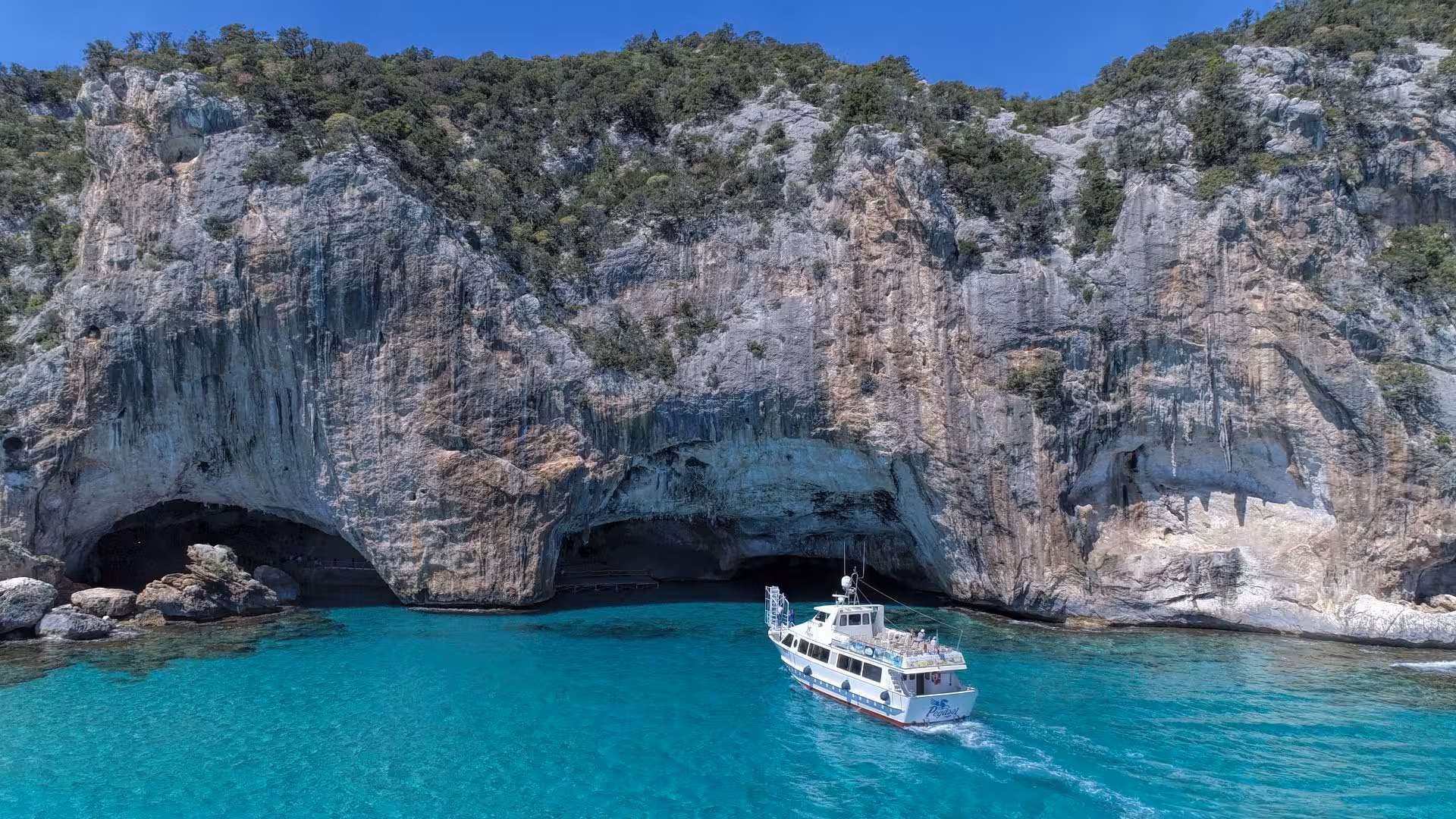 Scenic motorboat approaching the stunning Bue Marino Caves near Cala Gonone, Sardinia, with crystal-clear turquoise waters.
