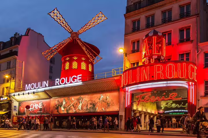 Iconic Moulin Rouge at night in Montmartre, Paris, featuring vibrant lights and bustling tourists on a full-day private tour.