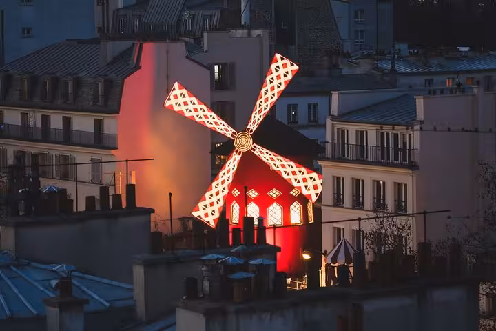 Illuminated Moulin Rouge windmill in Montmartre, Paris, featured on a street art walking tour with French drink tasting