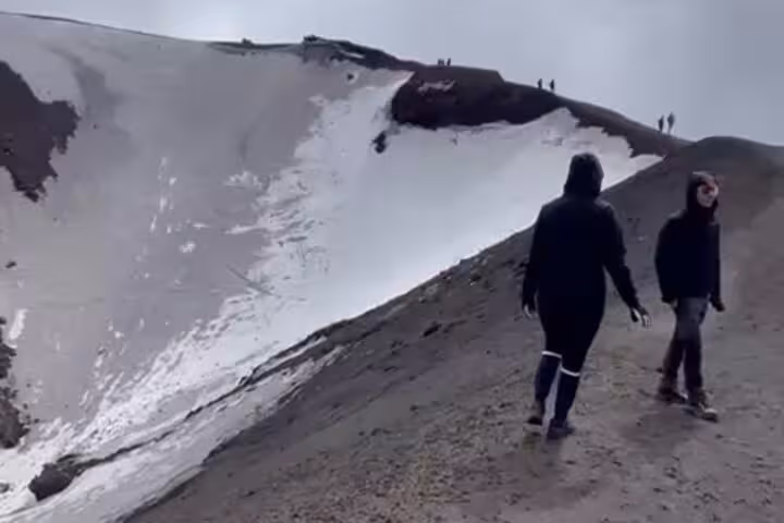 Hikers explore snow-dusted trails on Mount Etna under cloudy skies, highlighting adventure on the Etna Morning tour.