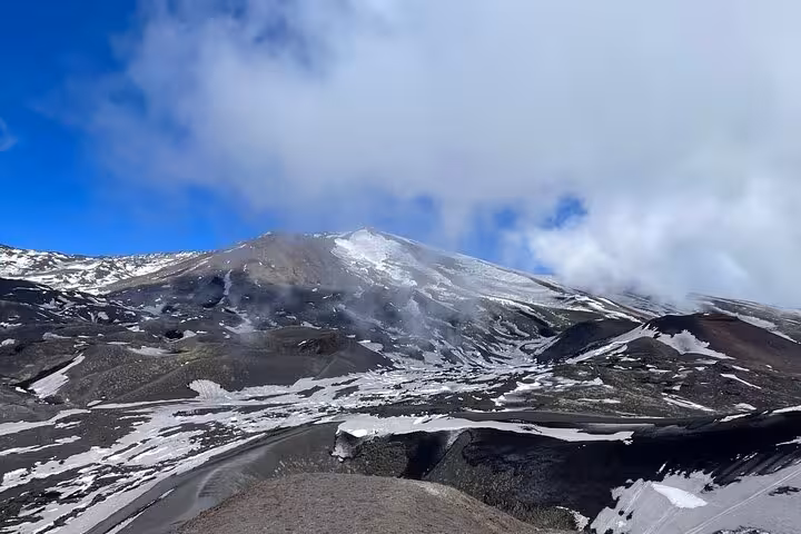 Snow-dusted slopes of Mount Etna with drifting clouds, showcasing the majestic volcanic landscape on a crisp morning.