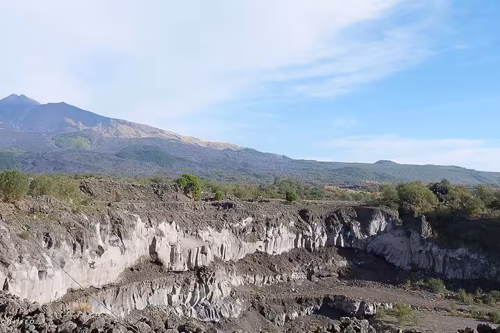 Breathtaking panorama of Mount Etna's rocky cliffs and lush surroundings, set against a serene sky backdrop.