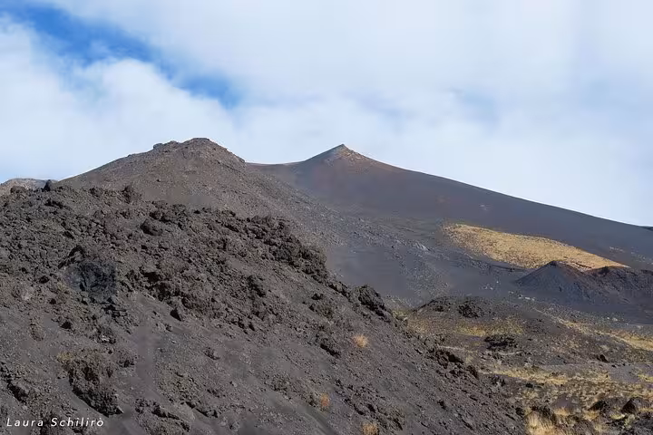 Expansive view of Mount Etna's rocky terrain with rugged slopes and a distant peak under a partly cloudy sky.