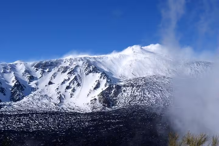 Snow-capped Mount Etna under a clear blue sky, showcasing its majestic volcanic peaks and pristine slopes.