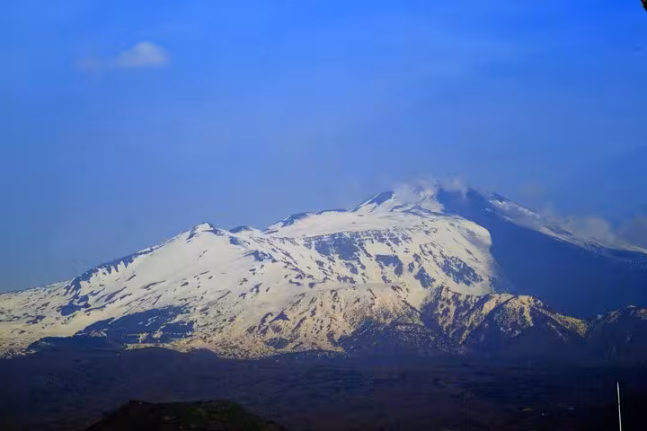 Aerial view of Mount Etna's snow-capped peaks under a clear blue sky, highlighting the stunning Sicilian landscape.
