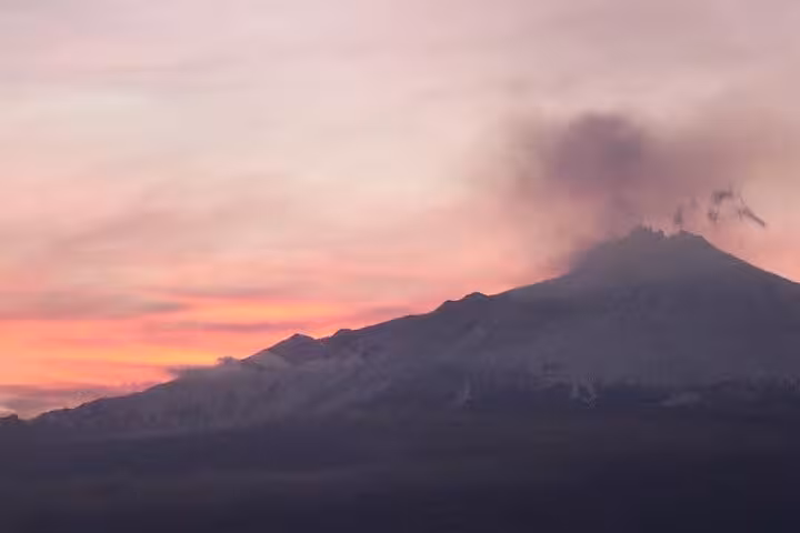 Mount Etna silhouetted against a vibrant sunset sky with smoke rising, offering a dramatic view on the Etna Sunset Tour.