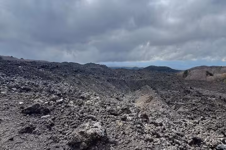 Rugged volcanic landscape of Mount Etna with rocky terrain and a cloudy sky, highlighting the dramatic scenery.
