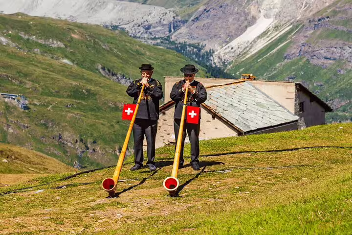 Traditional alphorn players with Swiss flags on a scenic hillside during Mount Pilatus & Lucerne private day trip.