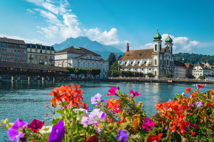 Vibrant flowers framing Lucerne's historic architecture with Mount Pilatus in the background on a sunny day.