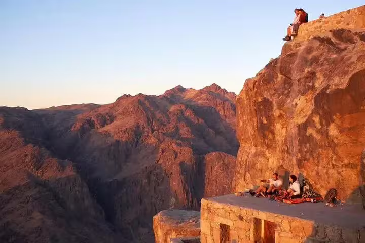 Travelers resting on Mount Sinai cliff at sunrise during private climb and St Catherine Monastery day tour