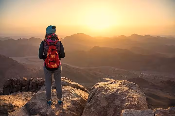 Hiker watching sunrise from Mount Sinai summit on Sharm El Sheikh day trip to St Catherine Monastery