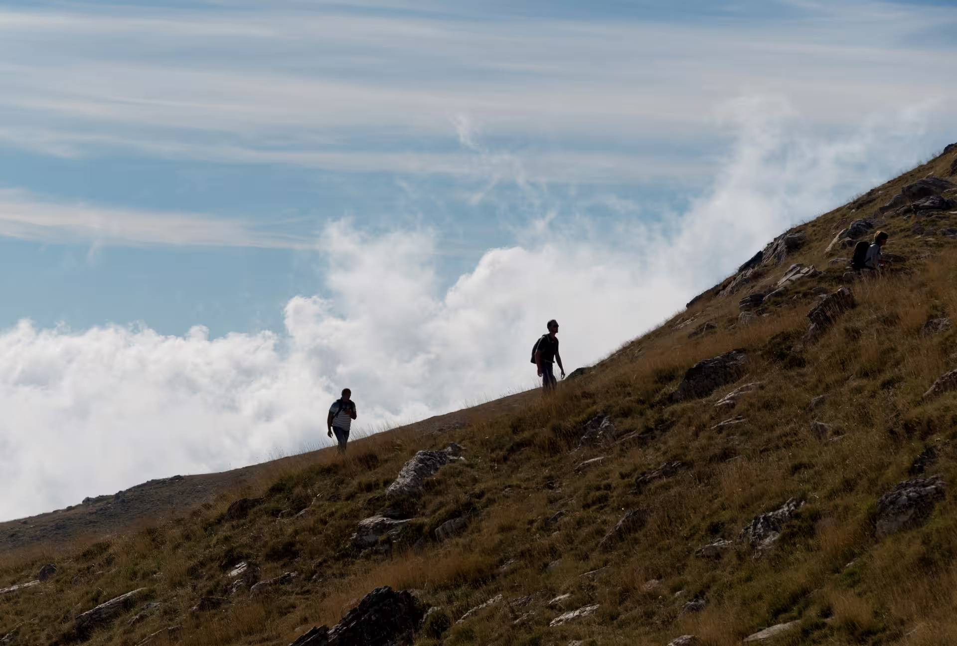 Hikers ascending a grassy ridge on Mount Taygetos, Greece, guided trek toward the 2407m summit above clouds