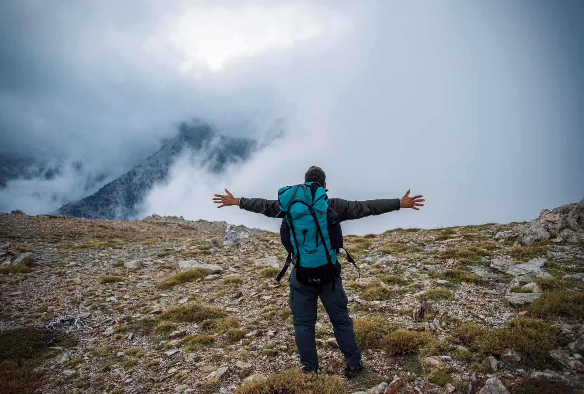 Backpacker with arms wide on Mount Taygetos high plateau, cloud views on 2407m summit hiking tour Greece